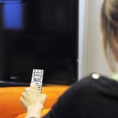 Nainen kaukosäädin kädessä television edessä.