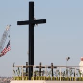 Paavi seisoo lavalla, jolla on suuri risti ja joukko pienempiä ristejä rajalla kuolleiden muistoksi. Taustalla liehuu Yhdysvaltain lippu nostokurjen nokassa.  