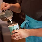 Kahvilatyöntekijä kaataa maitoa kahviin.