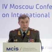 Kenraali Gerasimov seisoo puhujankorokkeen takana Moskovassa kansainvälisen turvallisuuden konferenssissa. Hänellä on yllään vihreä univormu, rintamuksessaan rivi kunniamerkkejä ja lehväkuviot kauluksissa.