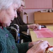 Vanha nainen syö piirakkaa pöydän ääressä