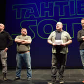 Neljä miestä seisoo näyttämöllä kertomassa Tahtien Sota -musiikkikomediasta