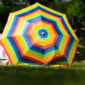 Sateenkaaren värinen päivänvarjo nurmikolla.
