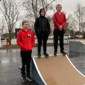 Kolme poikaa seisoo skeittirampilla koulun pihalla.