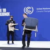 Työntekijät kantavat tuoleja lavalta ilmastokokouksen päätyttyä.