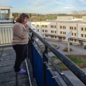 Nainen katsoo pihalle ylimmän kerroksen parvekkeeltaan.