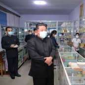 Kim Jong-un on kuvassa etualalla. Hänen takanaan näkyy apteekin työntekijöitä. 