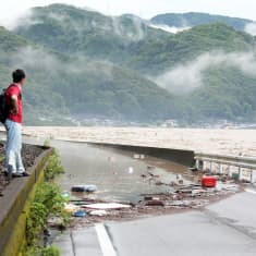 Mies katsoo tielle tulvinutta jokea Japanin Yatsushirossa
