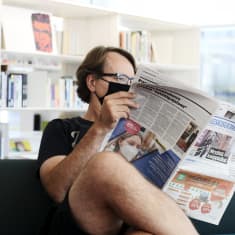 Mies maski kasvoillaan lukee Keskisuomalainen-sanomalehteä keskustakirjasto Oodissa.