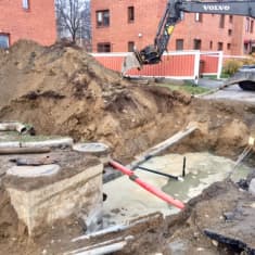 Kaivinkone kaivaa maata, kuvassa näkyy myös putkia.