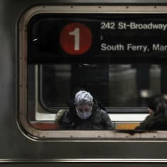 Kasvomaskiin pukeutunut matkustaja New Yorkin metrossa.