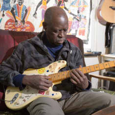 Senegalilainen muusikko Badu Ndjai soittaa nojatuolissa kitaraa.