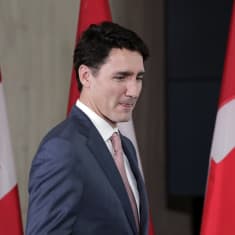 Kuvassa Kanadan pääministeri Justin Trudeau. Hänen takanaan on kolme Kanadan lippua. 