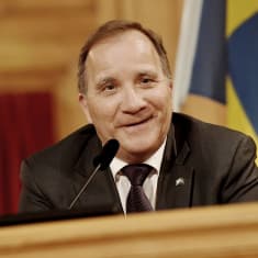 Hymyilevä Löfven taustallaan Ruotsin lippu.