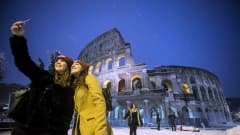 Turistit valokuvaavat lumisen Colosseumin edustalla  Roomassa.