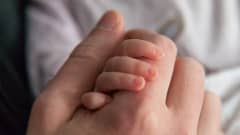 Vauva pitää kiinni isän kädestä.