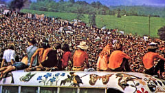 Yleisöä vuoden 1969 Woodstockin rockfestivaaleilla. Edessä olevat ihmiset istuvat bussin katolla.