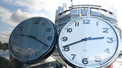 Käsi pitää kelloa ja Euroopan parlamenttirakennus Strasbourgissa siintää taustalla.