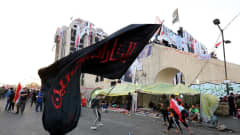 Nuori mies heiluttaa kadulla suurta mustaa lippua, jossa on punaista arabiankielistä kirjoitusta.