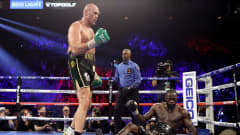 Tyson Fury seisoo kehässä, Deontay Wilder istuu.