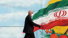 Mies kävelee Iranin lippua esittävän muraalin ohi.