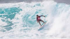 Kuvassa surffaaja, jonka asussa on punaista ja sinistä. Meressä on suuri aalto. 