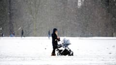 Nainen seisoo lastenvaunujen kanssa lumisateessa.