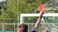 Kuvassa jalkapallotuomarin käsi on nostanut punaisen kortin ilmaan. 