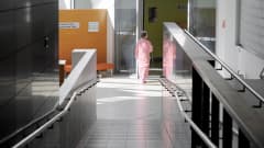 Sairaalan pyjamaan pukeutunut nainen kävelee sairaalan käytävällä.