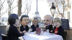 Neljä henkilöä suuret suurjohtajia esittävät maskit päässään syömästä lounasta.