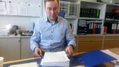 Rikoskomisario Petri Savela Oulun poliisilaitoksella työhuoneessaan pöydän ääressä taustalla kirjahyllyssä mappeja.