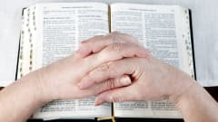 Naisen kädet ristissä raamatun päällä.
