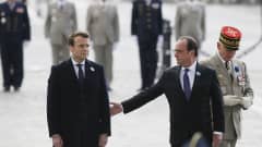 Hollande ojentaa kättä varautuneelle Macronille, taustalla univormupukuisia veteraaneja.