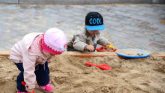 Kaksi lasta leikkii leikkipuiston hiekkalaatikolla.