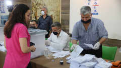 Nainen seisoo pöydän edessä, toisella puolella kasvomaskilla suojautunut vaalivirkailija nostelee äänestyslipukkeita