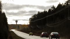 Kolme autoa ajaa jonossa maantiellä. Horisontissa näkyy Uudenkarlepyyn vesitorni.