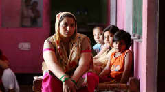 Kavita Gautam istuu roosan värisessä huoneessa kolmen lapsensa kanssa.