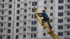 Kiinalainen siirtotyöläinen on kurottautunut kokoamaan metallisia rakennustelineitä Kiinan Pekingissä. Taustalla rakenteilla oleva betoninen kerrostalo.