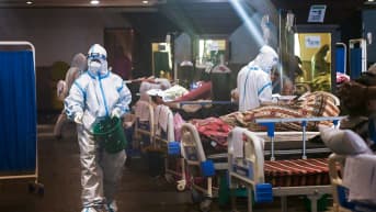 Suojavarusteisiin pukeutuneet työntekijät hoitavat sairaalasängyissä makaavia potilaita.