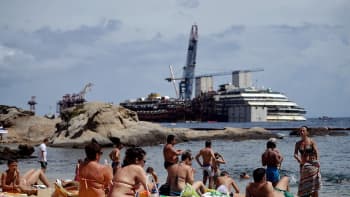 Ihmisiä rannalla Giglion saarella 26. kesäkuuta 2014 - edustalla haaksirikkoutunut Costa Concordia. 