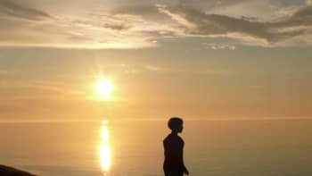 Poika kahlaa järven rannassa auringonlaskun aikaan
