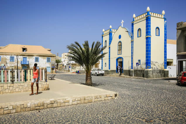 Kylän keskusaukio, jolla on kirkko, mukulakivikadut ja palmupuu.
