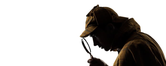 Sherlock Holmes -hahmo katsoo suurennuslasilla kannettavaa tietokonetta