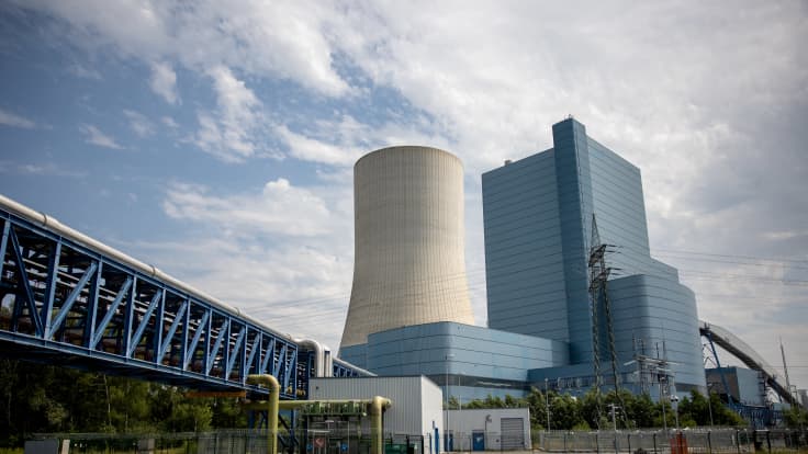 Valtava ydinvoimalan jäähdytystorni kuvattuna kanaalin yli kirkasta taivasta vasten.