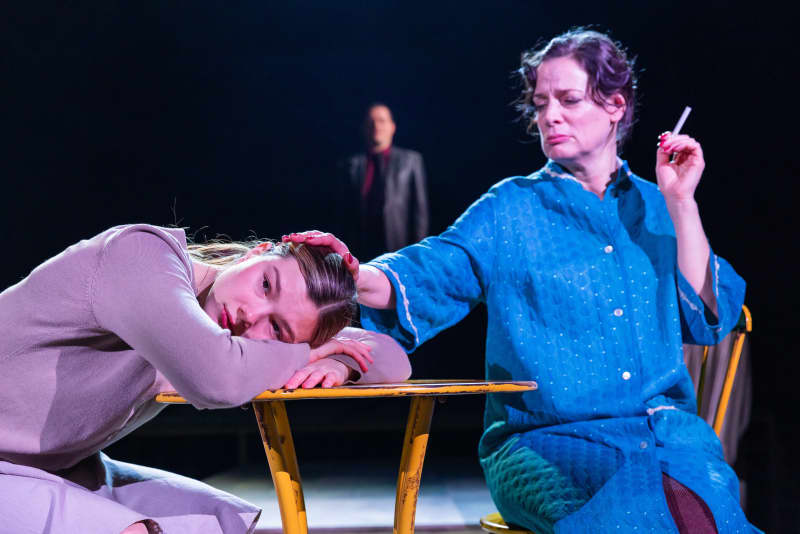 A woman sits and keeps her head on the table, the woman sitting opposite holds her hand on her head.