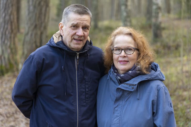 Olli (left) and Riitta Jalonen stand side by side in the forest and look at the camera.