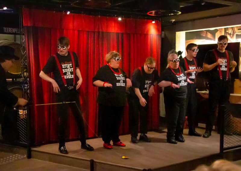 The picture shows seven actors on stage wearing funny glasses.