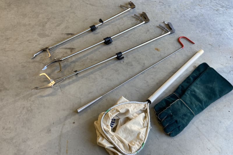 On the floor are three long metal pliers, a metal stick with a red hook at the end, a ghost and blue, thick gloves.