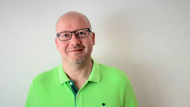 Доцент медіакультури Рамі Мехка посміхається на тлі білої стіни.