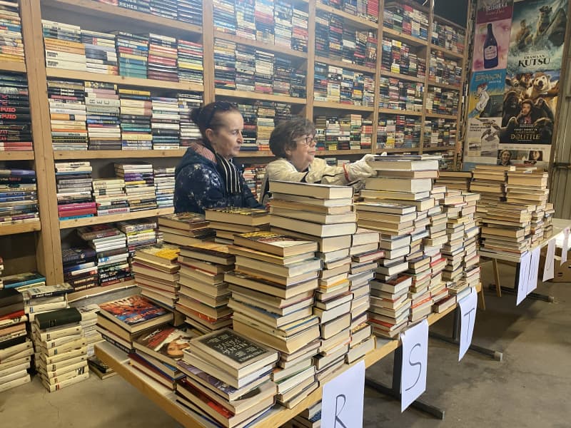 Two women are sorting through a large pile of books.